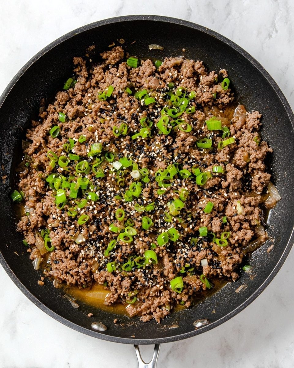 A black pan filled with one layer of cooked ground meat that is brown and crumbly, mixed with small pieces of translucent onions. On top, there are scattered small rings and pieces of bright green chopped spring onions along with a sprinkling of black and white sesame seeds. The pan is placed on a white marbled surface, showing some liquid juices pooling slightly around the edges of the meat. Photo taken with an iphone --ar 4:5 --v 7