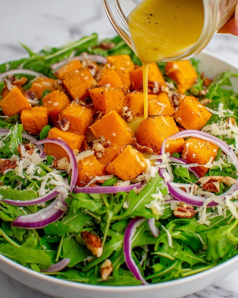 A white plate filled with a fresh salad shows three main layers: at the bottom is a base of dark green arugula leaves, giving a leafy texture; on top of that are bright orange roasted cubes, likely butternut squash, with a slightly soft surface and some browning marks; scattered throughout are thin slices of light purple onion and small pieces of brown walnut, adding contrast and crunch. A woman’s hand is seen pouring a golden yellow dressing from a small jar directly over the salad, with the liquid dripping down onto the layers below. The plate rests on a white marbled surface. photo taken with an iphone --ar 4:5 --v 7