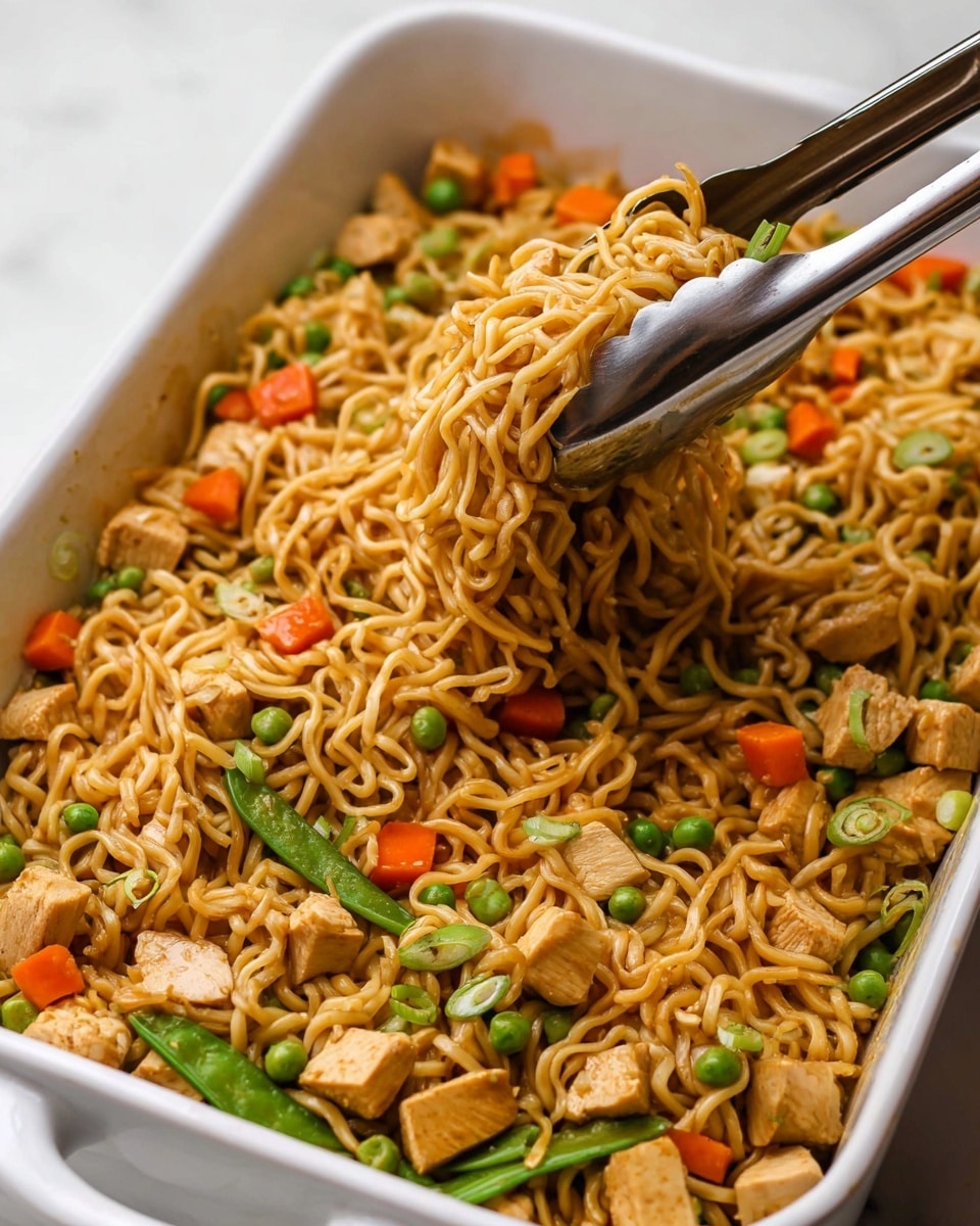 A white rectangular baking dish filled with stir-fried noodles mixed with small cubes of light brown cooked chicken, bright orange diced carrots, green peas, and whole green snap peas. The noodles are wavy and coated in a light brown sauce, with some green onion pieces sprinkled on top. A shiny metal tong is lifting a portion of noodles from the right side of the dish, showing the texture and slight gloss of the noodles. The dish sits on a white marbled surface photo taken with an iphone --ar 4:5 --v 7