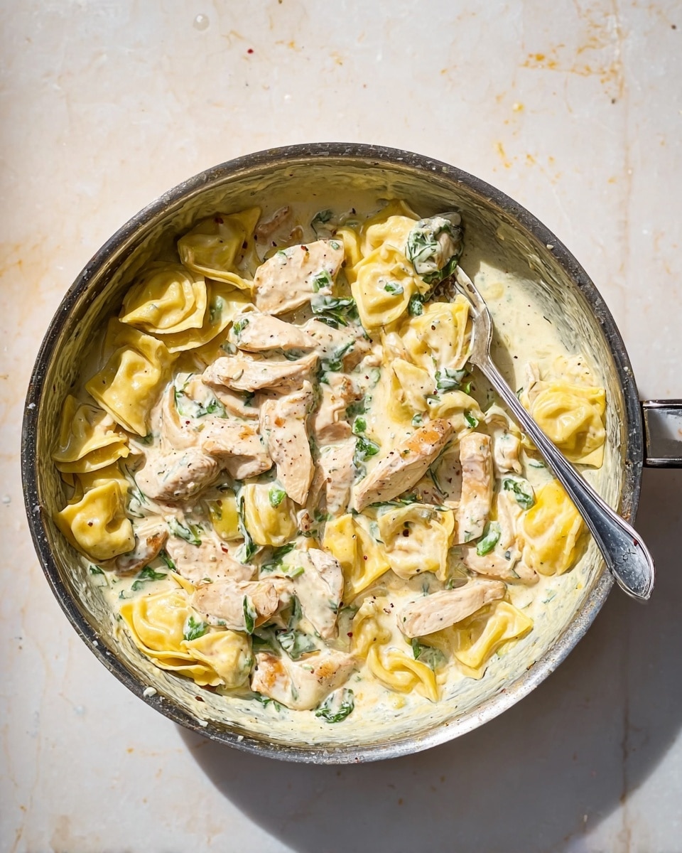 A metal pan filled with three layers: the bottom layer is creamy white sauce with some green leafy pieces mixed in, the middle layer consists of yellow ravioli pasta with a soft, smooth texture, and the top layer has several pieces of light brown cooked chicken strips scattered across. Some pasta and sauce coat the sides of the pan, and a silver fork rests inside on the right side. The pan is placed on a white marbled surface with soft shadows. photo taken with an iphone --ar 4:5 --v 7