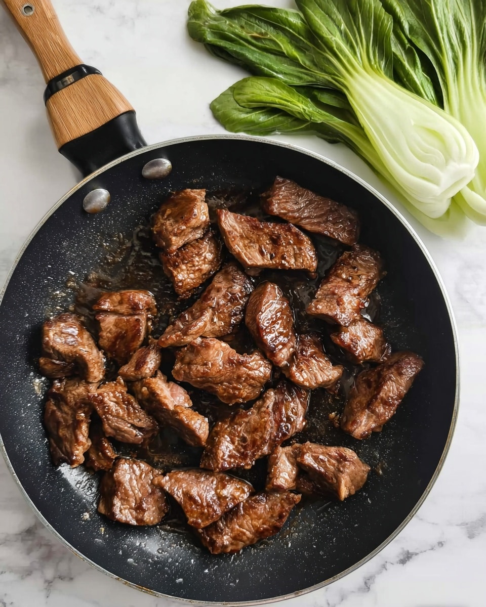 The image shows a black pan filled with pieces of cooked meat that are shiny and brown. The meat pieces have a slightly uneven shape and appear tender with a glossy, rich brown coating. The pan has a wooden handle that extends out of the top left corner of the image. At the top right of the pan, fresh green leafy vegetables with white stalks rest against the side of the pan, their bright green color contrasting with the deep brown of the meat. The background is a white marbled surface with a white and black checkered towel partially visible under the pan handle. photo taken with an iphone --ar 4:5 --v 7