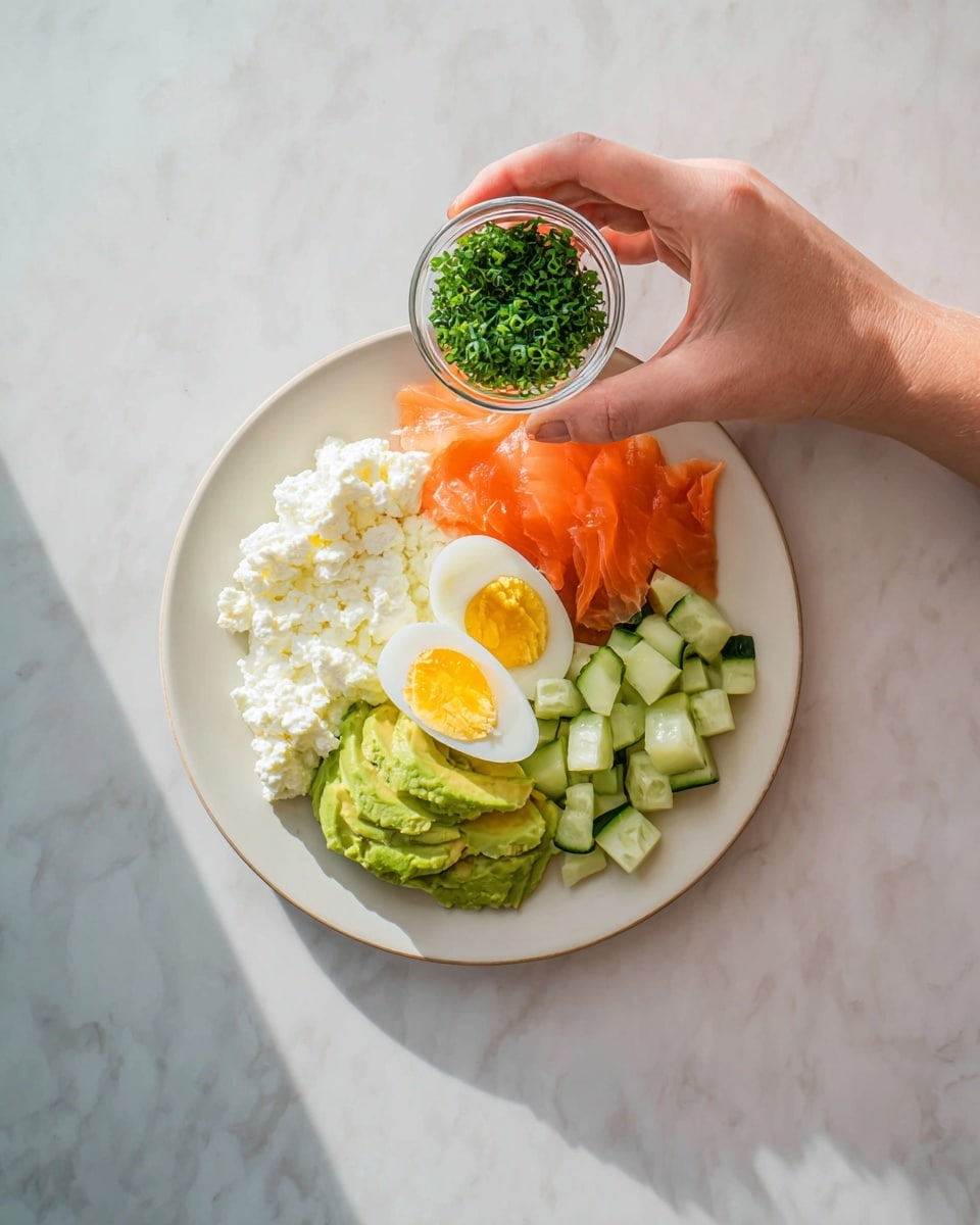 A white plate sits on a white marbled surface, filled with four main layers arranged side by side: creamy white cottage cheese on the left, bright green sliced avocado below it, a halved boiled egg with a yellow yolk in the middle, fresh orange slices of smoked salmon at the top right, and diced light green cucumber pieces on the far right. A woman's hand holds a small clear glass bowl filled with finely chopped green chives above the plate. The lighting is bright and natural, highlighting the fresh, colorful ingredients photo taken with an iphone --ar 4:5 --v 7