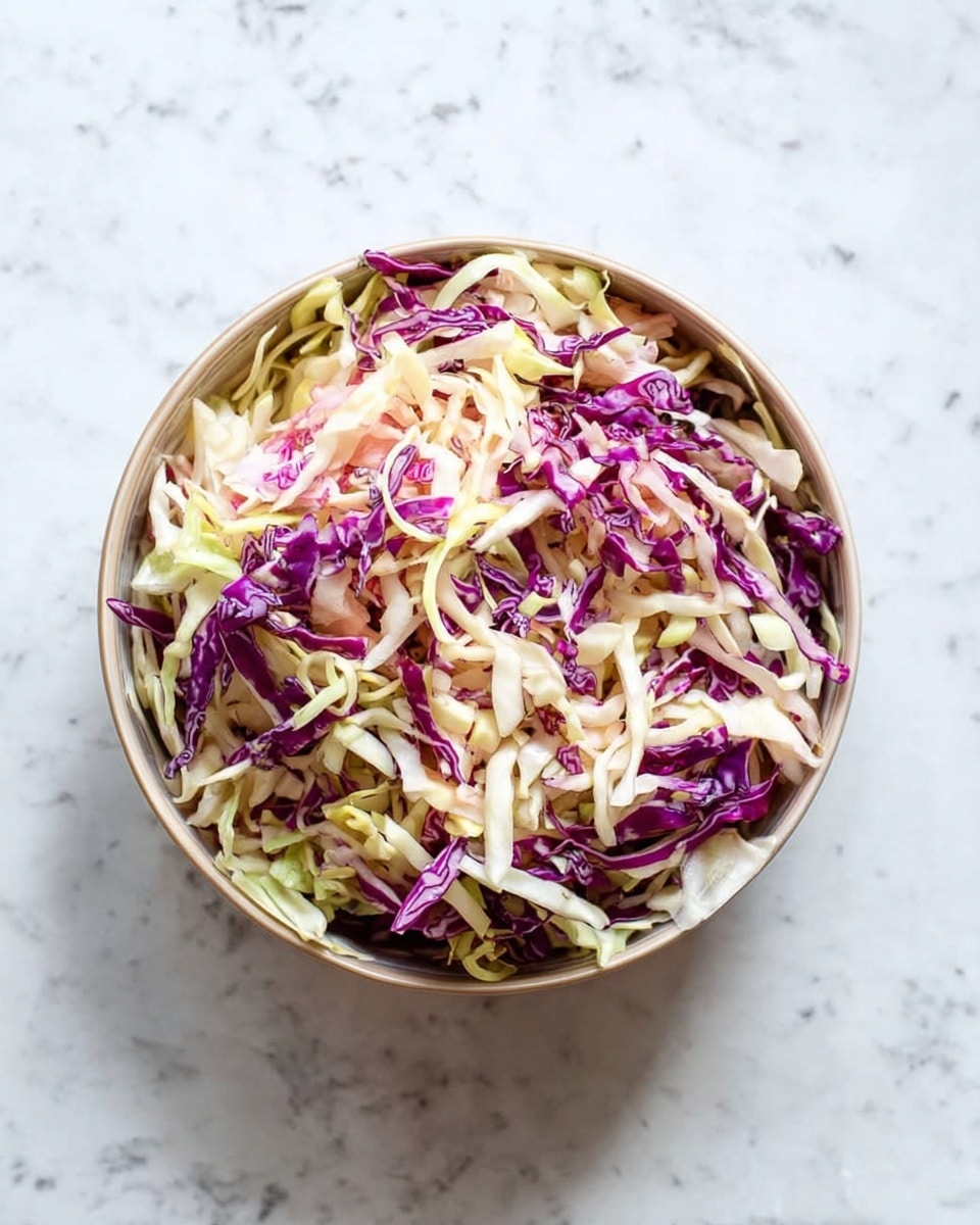 A round bowl filled with a colorful mix of shredded cabbage, featuring pale green, creamy white, and vivid purple strands. The shredded cabbage creates a textured and layered look, with the purple pieces standing out among the lighter colored ones. The bowl is placed on a white marbled surface that adds a soft contrast to the vibrant cabbage colors. photo taken with an iphone --ar 4:5 --v 7