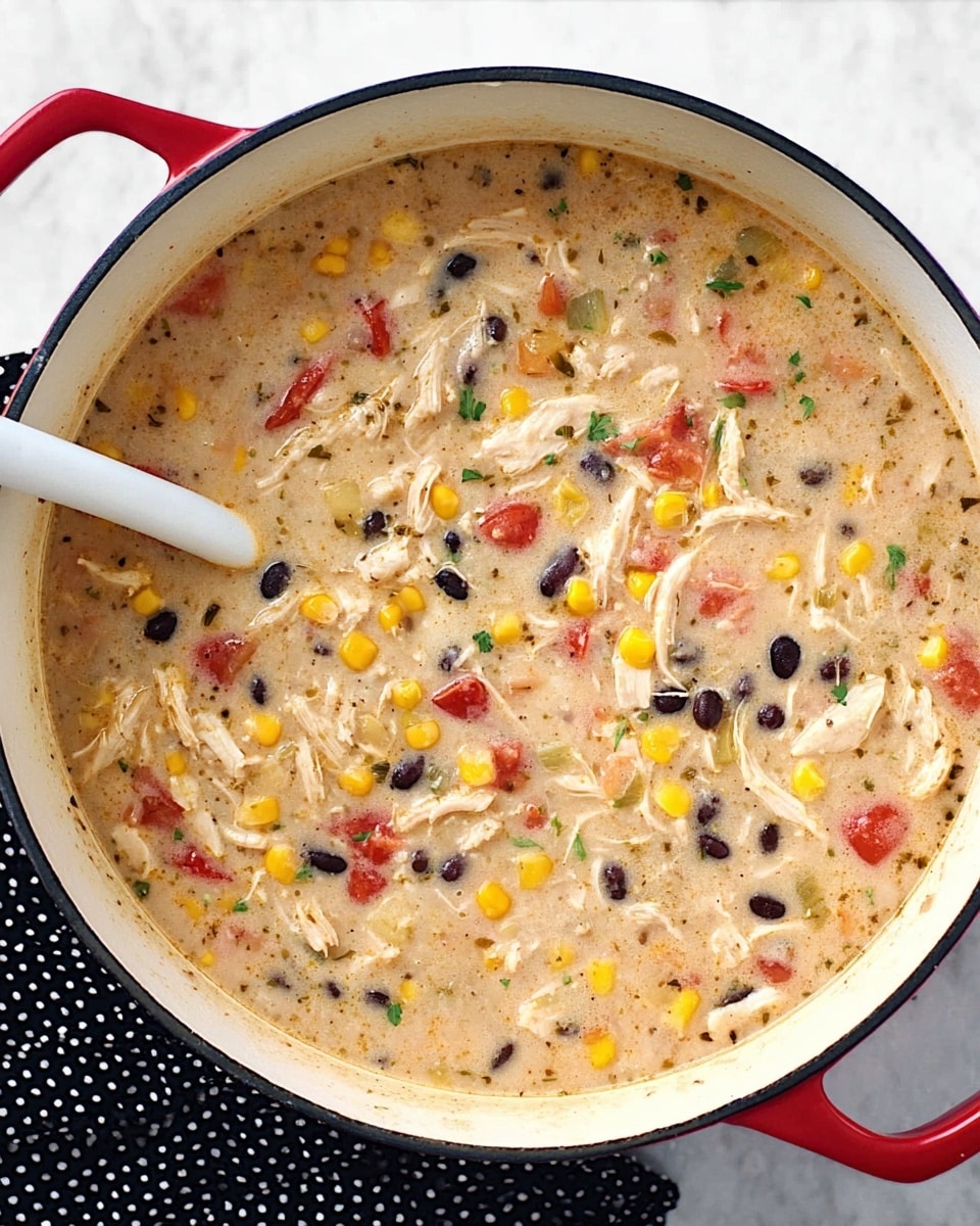 A white pot with a red rim is filled with a thick soup showing many layers of ingredients mixed together. The base is creamy light beige with chunks of shredded white meat spread evenly through it. Bright yellow corn kernels dot the soup along with small black beans and pieces of red tomato. There are hints of green herbs scattered around, giving a fresh touch. A white spoon dips into the soup from the left side. The pot is on a white marbled surface with a black and white polka dot cloth nearby. Photo taken with an iphone --ar 4:5 --v 7
