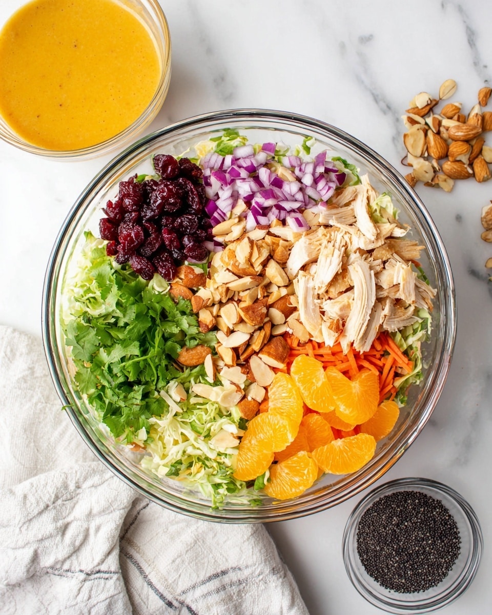 A clear glass bowl on a white marbled texture holds a colorful layered salad. The bottom layer is light green shredded cabbage mixed with thin carrot strips. On top, starting from the left, there are dark red dried cranberries, light purple chopped onions, light brown sliced almonds, bright green chopped cilantro in the center, golden brown crunchy pieces, light beige shredded chicken on the top right, and bright orange mandarin slices at the bottom right. Nearby on the white marbled surface is a small clear bowl filled with black poppy seeds and a glass cup of orange dressing. A white and gray cloth is partially under the bowl. Photo taken with an iphone --ar 4:5 --v 7