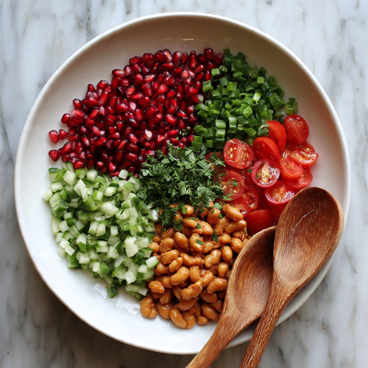 A white bowl with six colorful sections of fresh ingredients arranged side by side. Starting from the top left, there are bright red pomegranate seeds, small chopped dark green green onions to the right, and bright red cherry tomato halves next to them. Below the tomatoes, there are light brown roasted beans, and below the beans and to the left, there are medium green chopped cucumber pieces. In the center is a small pile of finely chopped fresh green herbs. A wooden spoon rests inside the bowl on the right side, with another wooden spoon placed on top of the bowl. The bowl is set on a white marbled surface. Photo taken with an iphone --ar 4:5 --v 7