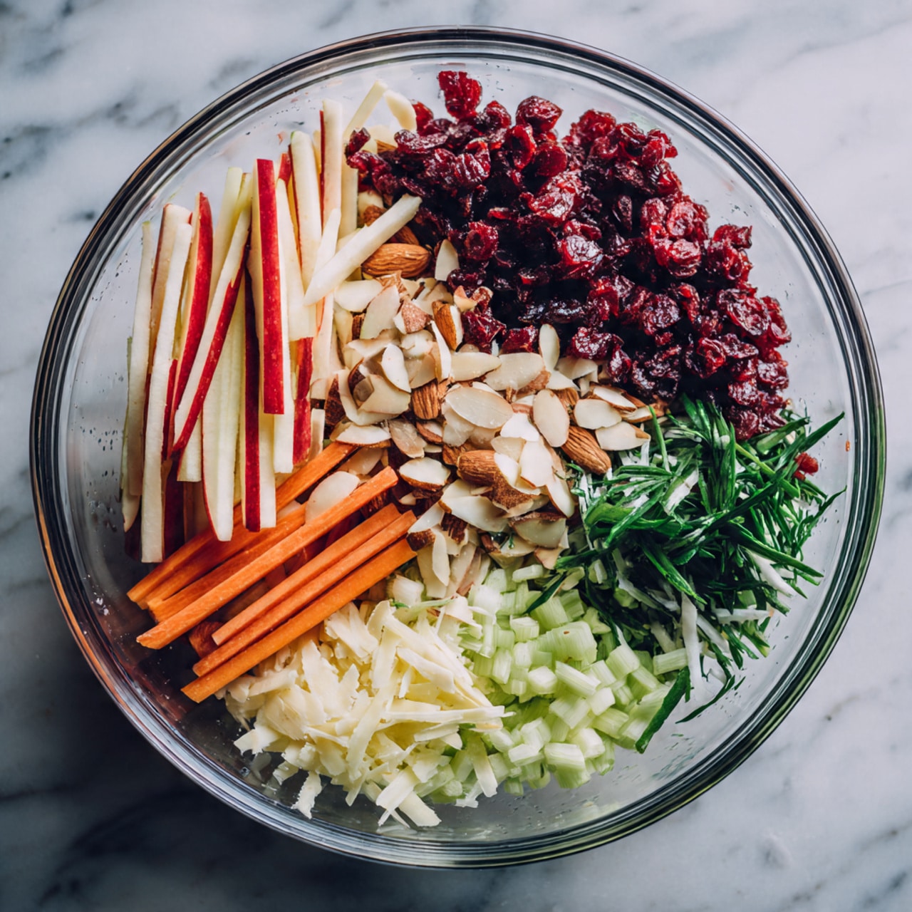 A clear glass bowl holds five neat layers of fresh ingredients arranged side by side in a circle. At the top right, there is a layer of thin, long red and white apple sticks with smooth edges. Next, to the left is a pile of shiny dark red dried cranberries. On the far left, there are pale brown thin almond slices with a slightly rough texture. Below the almonds is a bright green shredded leafy vegetable, and just beneath it, a layer of chopped green onions with a glossy finish. At the bottom right, carrot sticks with a vibrant orange color fill the last section, contrasting with the greens and reds. The bowl sits on a white marbled surface photo taken with an iphone --ar 4:5 --v 7
