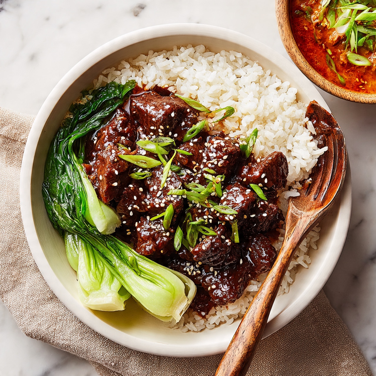 A white bowl filled with three main layers: the base is a bed of white rice, fluffy and slightly separated; on one side, two bright green bok choy pieces with a slight shine and some sesame seeds sprinkled on top; in the center, a generous portion of dark brown, tender braised meat covered in a thick, shiny dark sauce, topped with thinly sliced green onions and toasted sesame seeds; a wooden fork rests on the edge of the bowl with a piece of meat on it. The bowl sits on a beige cloth over a white marbled surface, with a second bowl partially visible in the background holding a reddish-orange sauce garnished with green onion slices. Photo taken with an iphone --ar 4:5 --v 7