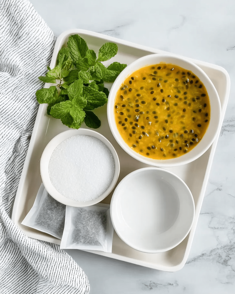 A white rectangular tray holds several items arranged neatly on a white marbled surface. On the tray, there is a white round bowl filled with bright yellow-orange passion fruit pulp dotted with small black seeds, showing a slightly wet and textured surface. Next to it is a small white bowl full of fine white granulated sugar, smooth and level. Above these, there is an empty white round bowl with a smooth texture. To the left of the sugar bowl, there are fresh green mint sprigs with bright leaves. At the bottom left corner of the tray, there are three tea bags with white paper covers and visible dark contents inside. A white kitchen towel with thin black stripes is partly visible on the right edge of the tray. photo taken with an iphone --ar 4:5 --v 7