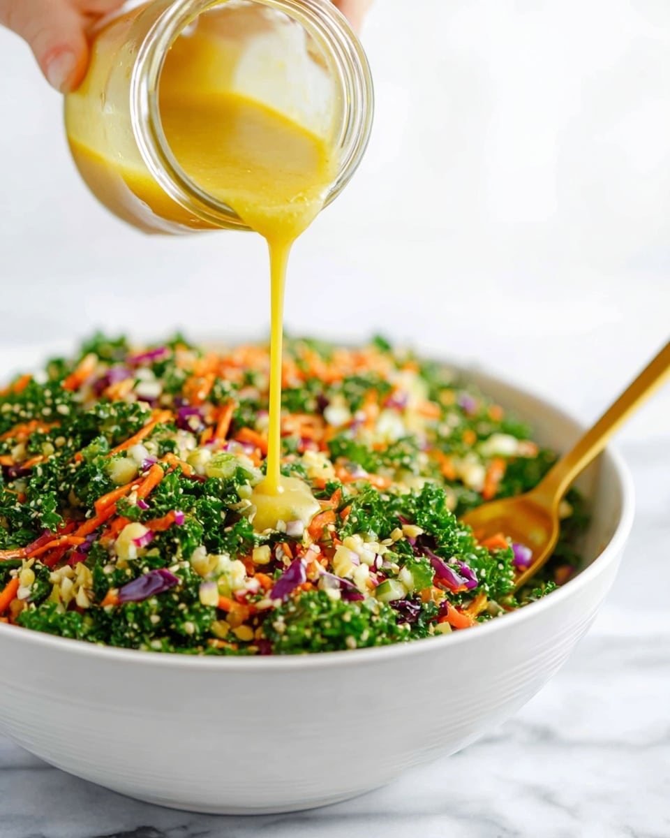 A close-up image shows a woman's hand pouring a thick, yellow dressing from a small glass jar over a large white bowl filled with a finely chopped salad. The salad contains multiple layers of green kale, small pieces of orange carrot, purple cabbage, and bits of light green broccoli, mixed evenly with some seeds. A gold spoon rests on the edge of the bowl, partially submerged in the salad. The background is a soft white marbled surface, giving a clean and bright look. Photo taken with an iphone --ar 4:5 --v 7