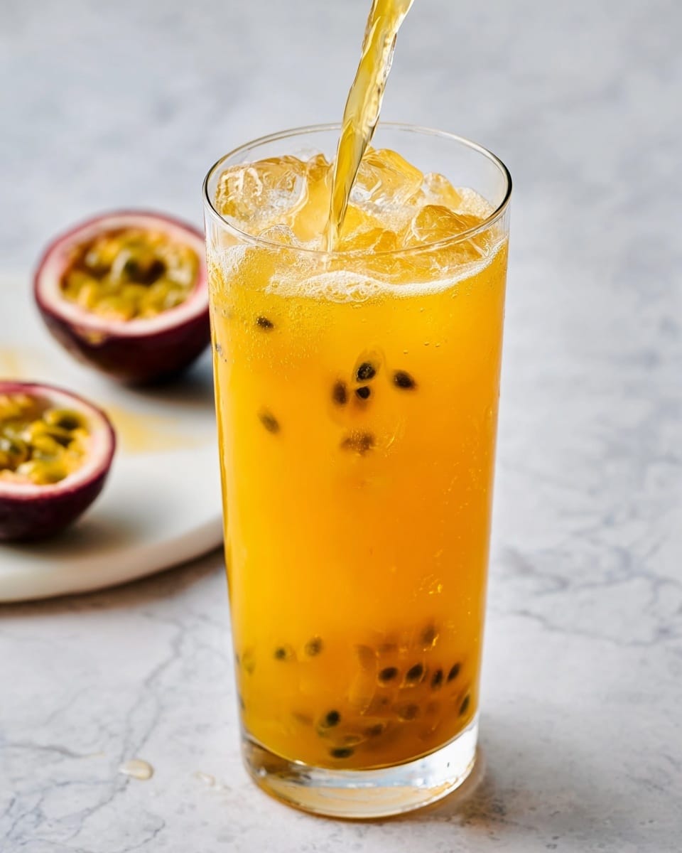 A tall clear glass is filled with bright orange passion fruit juice, with visible black passion fruit seeds floating near the top layer. There are several pieces of ice inside the glass, giving a cool, refreshing look. The juice is being poured from above, creating a splash and some bubbles at the surface. In the background, a halved passion fruit with bright yellow seeds is on a white marbled surface. The photo is bright and fresh, taken close up to show the texture of the drink and the seeds clearly photo taken with an iphone --ar 4:5 --v 7