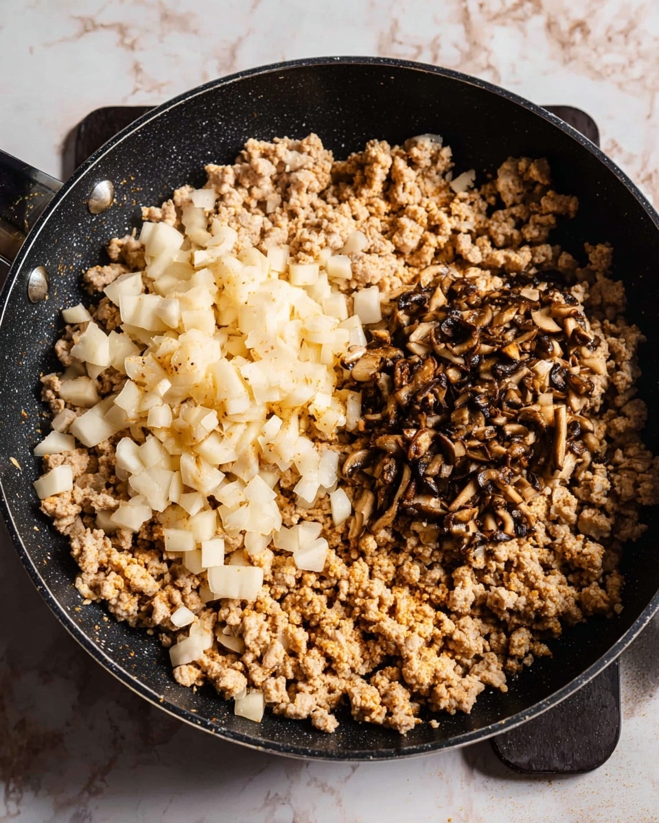 The image shows a black pan filled with three main layers of food. The bottom layer has light golden-brown cooked ground meat spread across the whole pan. On top of this, there are two piles of diced ingredients both near the center but separated—one pile is light cream-colored diced pieces, and the other pile is darker brown finely chopped pieces, likely mushrooms. The pan is placed on a dark square holder, and the background surface is a white marbled texture. photo taken with an iphone --ar 4:5 --v 7