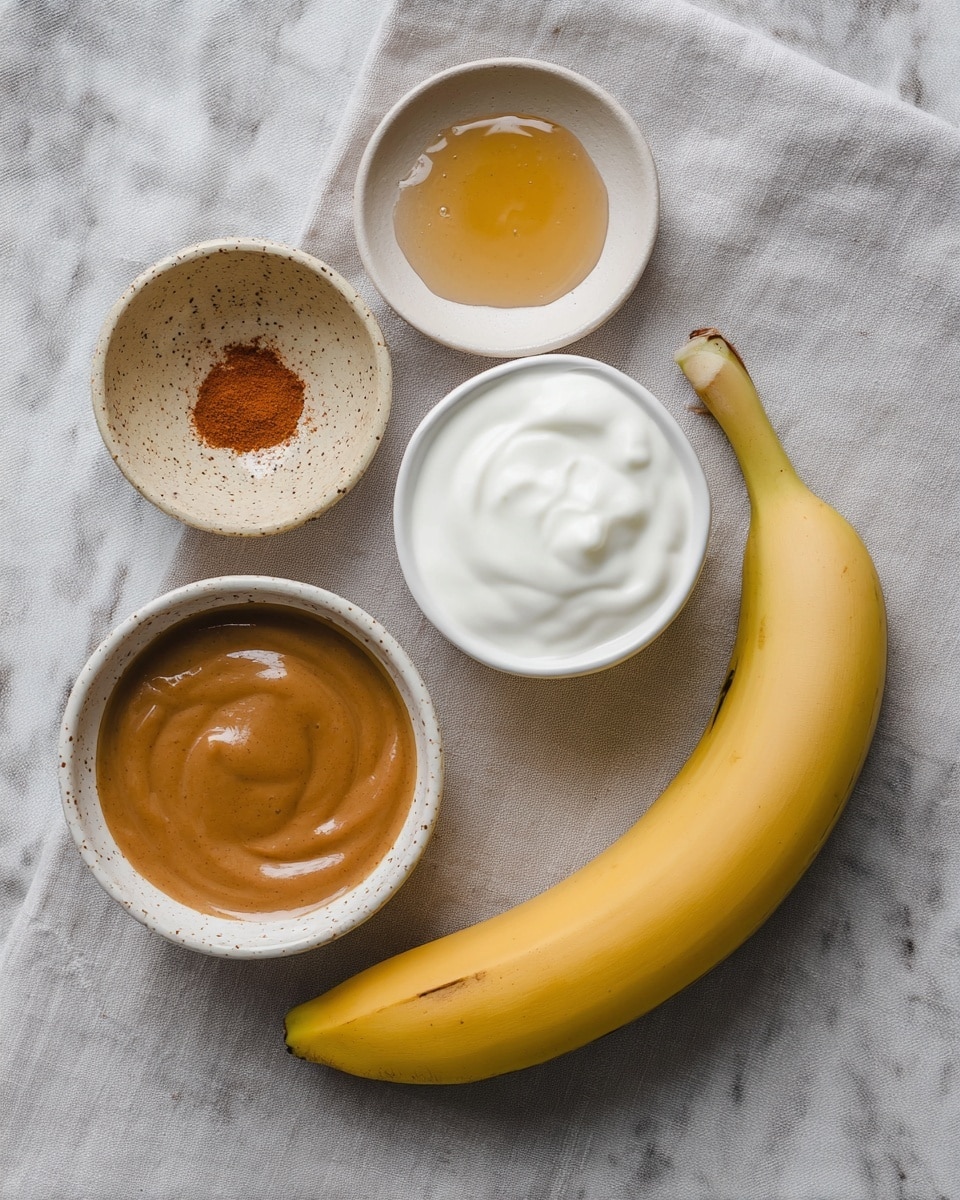 The image shows five items placed on a soft light gray cloth with a white marbled texture underneath. There is one whole yellow banana on the bottom right, curved slightly with a few small dark spots on its peel. Around the banana, there are four small bowls. The top right bowl contains smooth white yogurt. Below it, a white bowl filled with a smooth brown sauce sits. To the upper left, a small speckled beige bowl holds a dollop of honey with a shiny texture. Lastly, another small speckled beige bowl at the bottom left has a reddish-brown powder, likely a spice. The arrangement is simple and clean, with natural colors and soft light. photo taken with an iphone --ar 4:5 --v 7