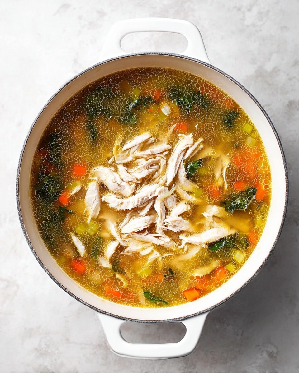 A white pot filled with a clear, golden broth that shows small bubbles, mixed with chunks of orange carrot, green leafy herbs, and light green celery pieces spread through the soup. On top, there is a pile of shredded white meat placed in the center, slightly overlapping some of the broth and vegetables. The pot is set on a white marbled surface with the handles visible on the sides, creating a clean and simple look. photo taken with an iphone --ar 4:5 --v 7
