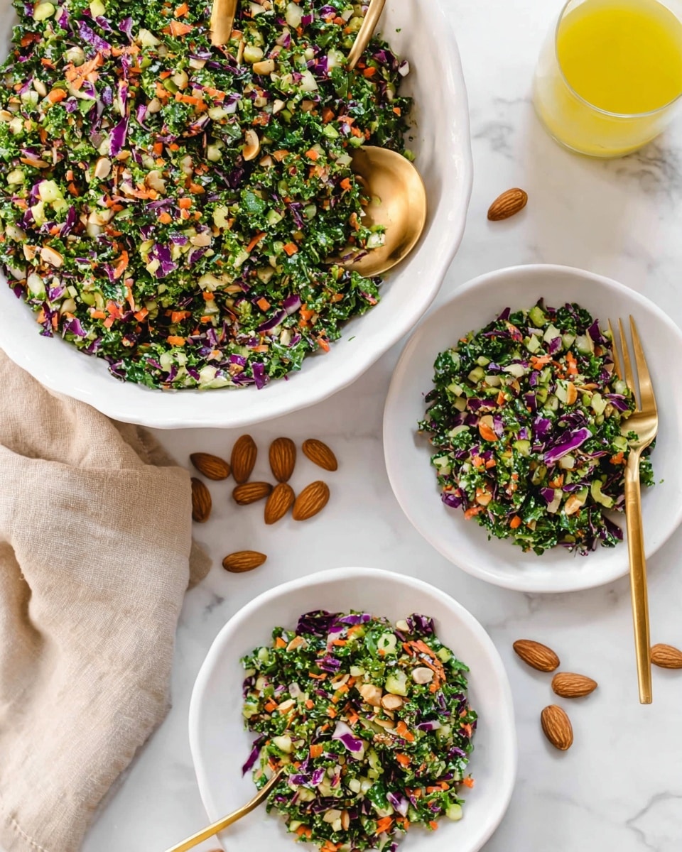 A large white bowl filled with a colorful mixed salad consisting of finely chopped greens including kale and purple cabbage, small pieces of orange carrot, and bits of light-colored nuts spread evenly throughout. Two smaller white plates hold similar portions of the salad, each showcasing bright green, purple, and orange pieces mixed together. A gold spoon rests inside the large bowl, and another gold utensil is placed on the bottom plate. Scattered almonds surround the dishes on a white marbled surface, with a glass of yellow dressing or juice visible to the side and a beige cloth partially showing. Photo taken with an iphone --ar 4:5 --v 7