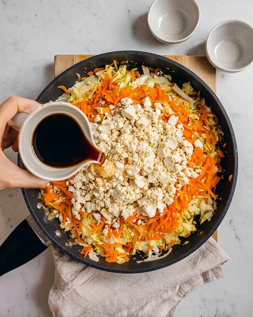 A black pan with a layer of cooked shredded orange carrots and light yellow cabbage spread evenly on the bottom, topped with a thick layer of crumbled white tofu. A woman's hand is pouring dark brown sauce from a small white cup onto the tofu. The pan is on a white marbled surface with a folded light cloth under it, and two small empty white bowls are placed nearby. The photo is taken with an iphone --ar 4:5 --v 7