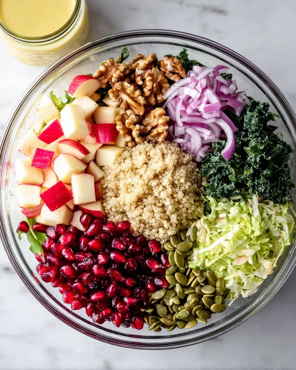 A clear glass bowl holds a colorful salad with seven distinct layers arranged in a circle. Starting from the top left, there are small red and white apple cubes, followed by light brown walnut pieces. Next to the walnuts are thin slices of purple-red onion, then dark green kale leaves. Below the kale is a pile of bright red pomegranate seeds, next to a fluffy mound of beige quinoa. Moving left, there are green pumpkin seeds, and finally, light green shredded lettuce. The bowl is placed on a white marbled surface, with a jar of light yellow dressing visible in the background. Photo taken with an iphone --ar 4:5 --v 7