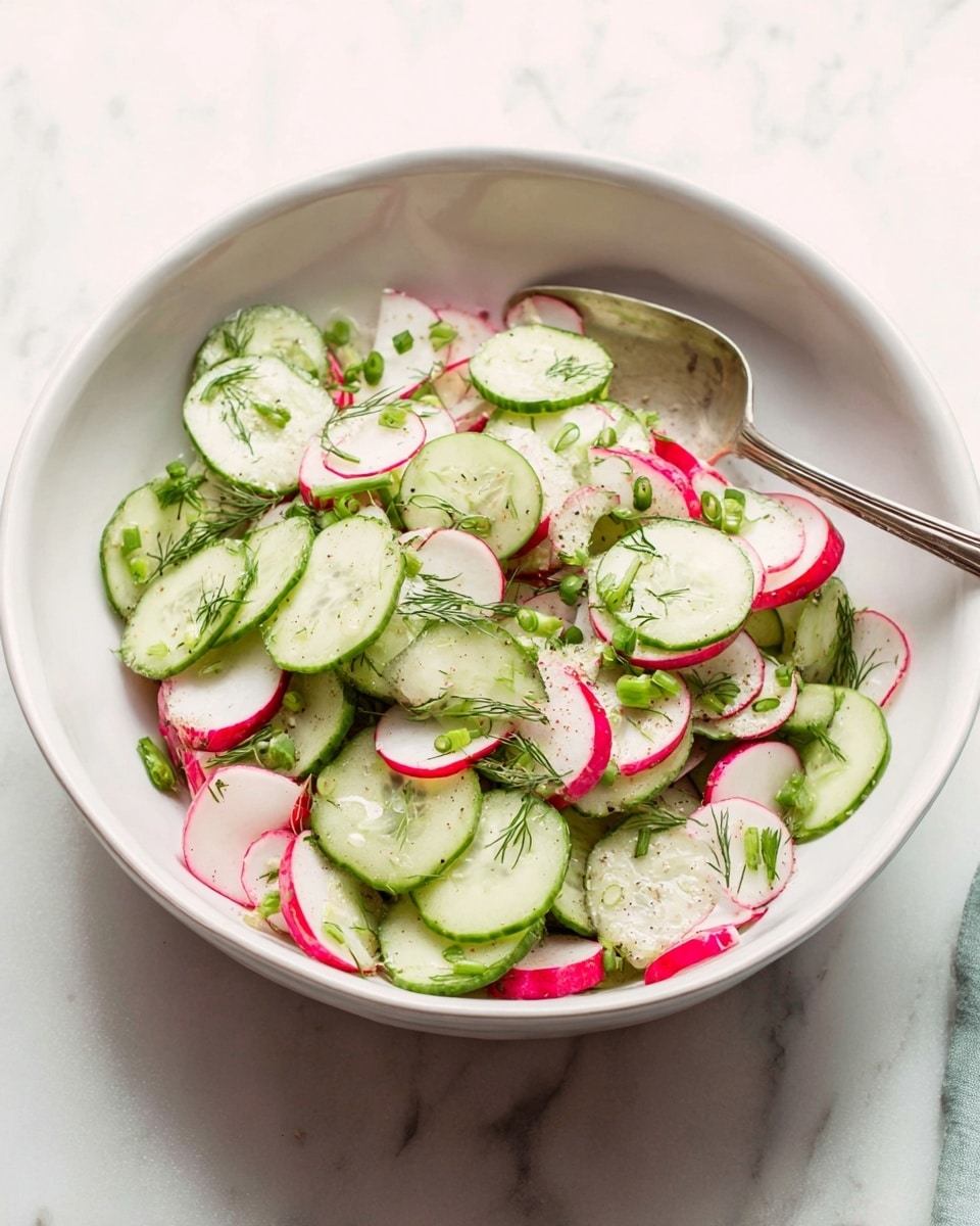 A bowl filled with thin, round slices of cucumber and radish mixed together evenly. The cucumbers are light green with darker green edges, showing a crisp texture, while the radish slices have a white center with bright pink edges. Small, finely chopped green onions are scattered across the top, along with tiny sprigs of dill adding a touch of green and texture. The bowl is white and smooth, placed on a white marbled surface, with a silver spoon resting inside the bowl. photo taken with an iphone --ar 4:5 --v 7