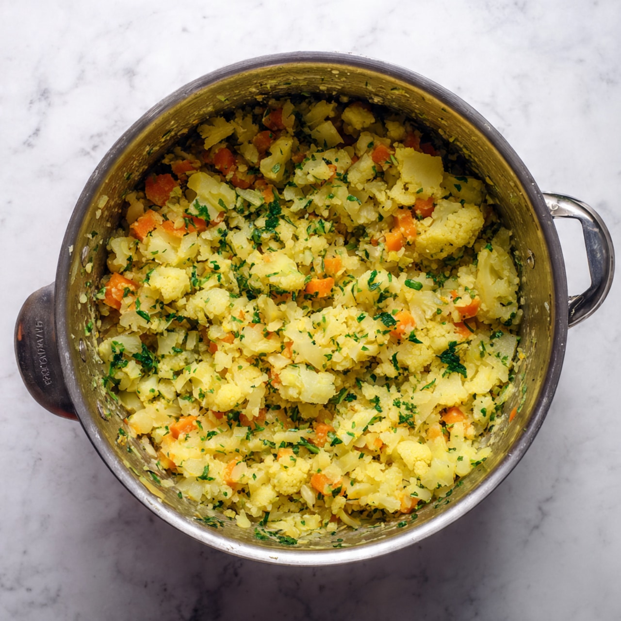 A close-up image of a cooking pot filled with a mixed dish made of finely chopped light yellow cauliflower pieces and small bright orange carrot cubes, with soft translucent onion bits spread throughout. The texture is moist and slightly soft, showing the mix is being sautéed or cooked. The inside surface of the pot is smooth and grey with a slight shine. The dish fills the pot unevenly with a sense of gentle stirring. The background is a white marbled texture. photo taken with an iphone --ar 4:5 --v 7