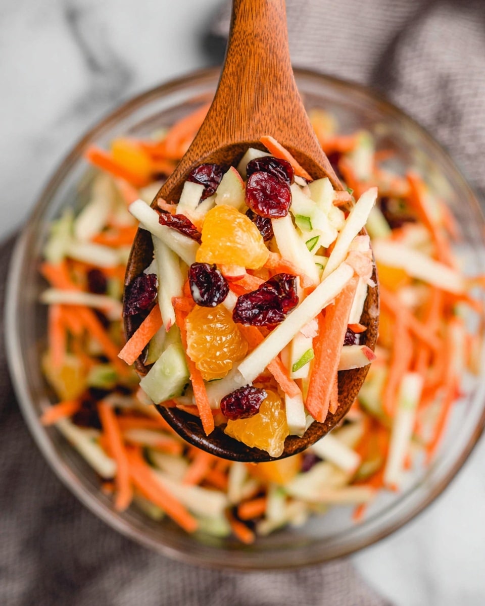 A close-up of a wooden spoon holding a colorful salad with three main layers: bright orange carrot sticks, pale white apple slices, and dark red dried cranberries on top; the salad also includes small chunks of orange mandarin and thin green cucumber pieces mixed throughout. The spoon hovers over a clear glass bowl filled with the same salad on a white marbled surface with a soft gray cloth nearby. The textures appear fresh and slightly glossy, showing the juicy and crisp nature of the ingredients. photo taken with an iphone --ar 4:5 --v 7