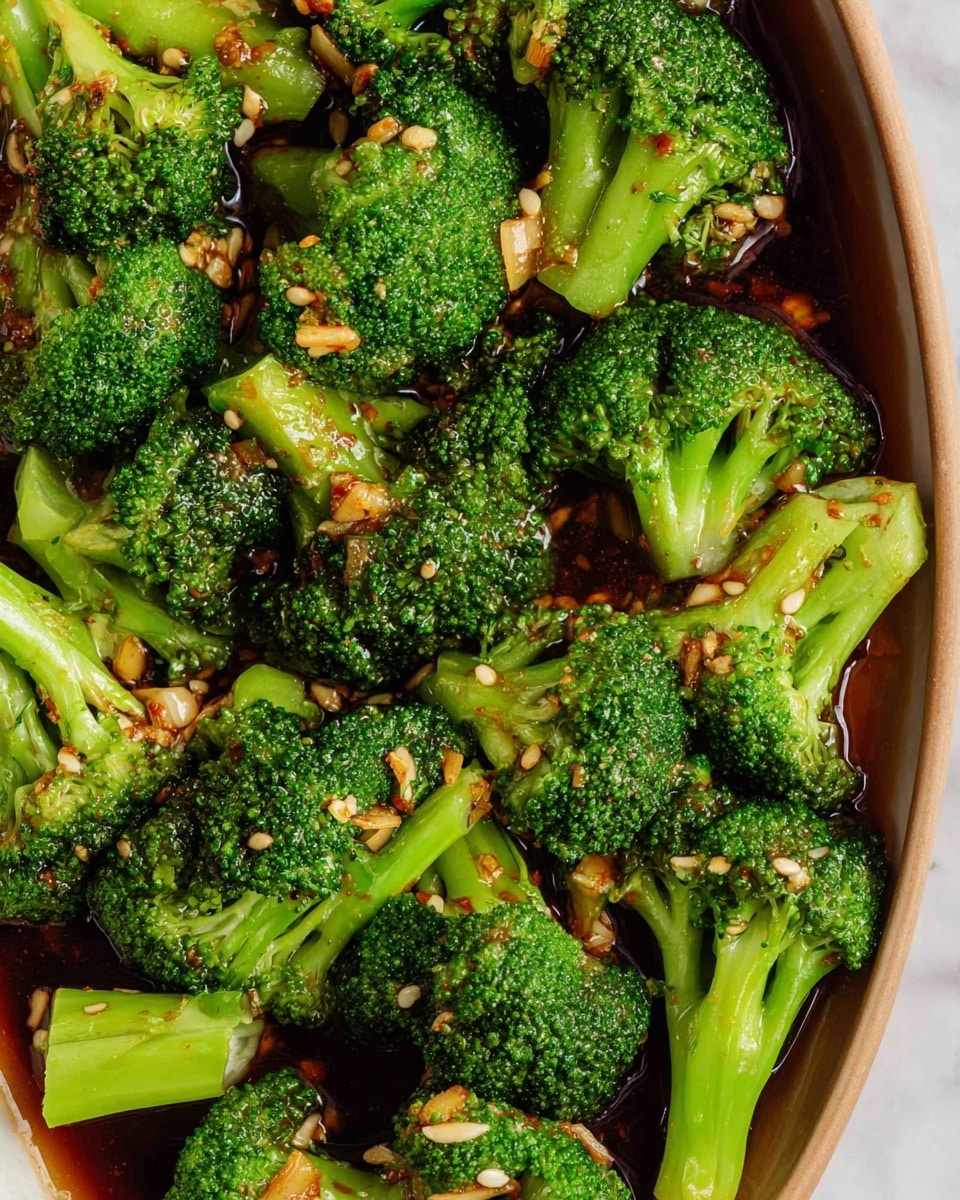 The image shows a close-up of cooked broccoli florets soaked in a dark brown sauce with small pieces of garlic and sesame seeds scattered on top. The broccoli is bright green with a slightly glossy look from the sauce. The pieces are uneven in size, showing both the dense, small buds on top and the thicker stems. The sauce pools gently around the broccoli, shining under the light on a white marbled surface. photo taken with an iphone --ar 4:5 --v 7