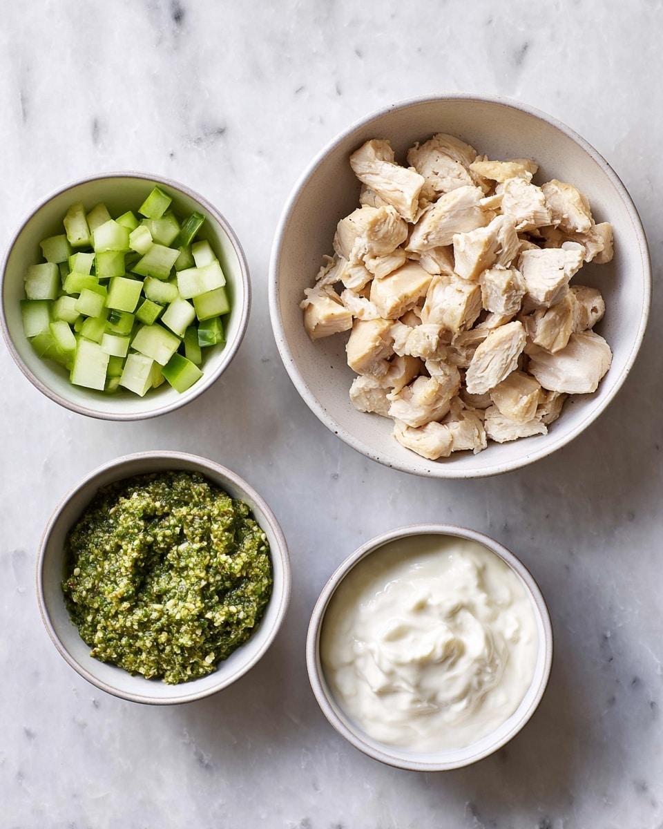 Four white bowls on a white marbled surface, arranged in a loose square. The largest bowl at the top right holds a pile of light beige cooked chicken pieces with a slightly rough texture. To the top left is a bowl filled with small, bright green diced cucumber pieces. Below that bowl is a smaller bowl with a coarse green pesto sauce that looks textured with bits of nuts and herbs. At the bottom right is another bowl with a smooth, thick white cream. photo taken with an iphone --ar 4:5 --v 7