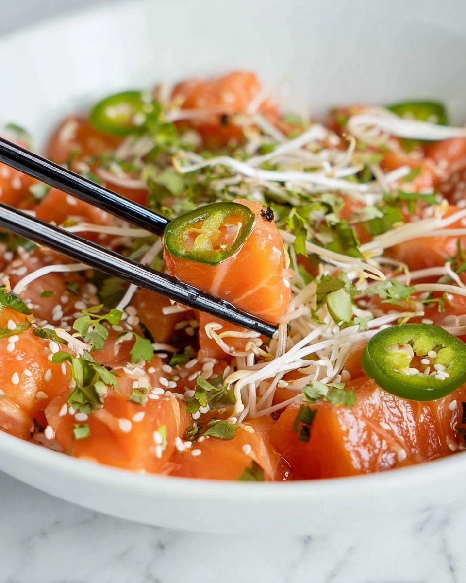 The image shows a white bowl filled with several layers of bright orange salmon chunks as the main layer, scattered with thin, white bean sprouts on top. There are also slices of green jalapeño peppers and small green herb leaves sprinkled throughout. Tiny white sesame seeds add a light texture on the surface. A pair of black chopsticks is holding a cube of salmon with a jalapeño slice on it, positioned near the center of the bowl. The bowl sits on a white marbled surface. photo taken with an iphone --ar 4:5 --v 7