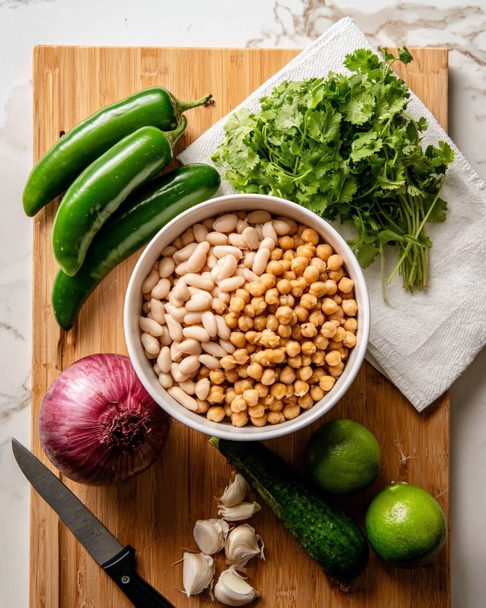 A white bowl filled with two layers of beans: a bottom layer of white beans and a top layer of light brown chickpeas, sits on a wooden cutting board. Around the bowl, there are three green chili peppers, one whole red onion, a bunch of fresh green cilantro on a white paper towel, a black-handled knife, a green cucumber, two whole limes, and five garlic cloves. All items are arranged neatly on the cutting board, which is placed on a white marbled surface. photo taken with an iphone --ar 4:5 --v 7