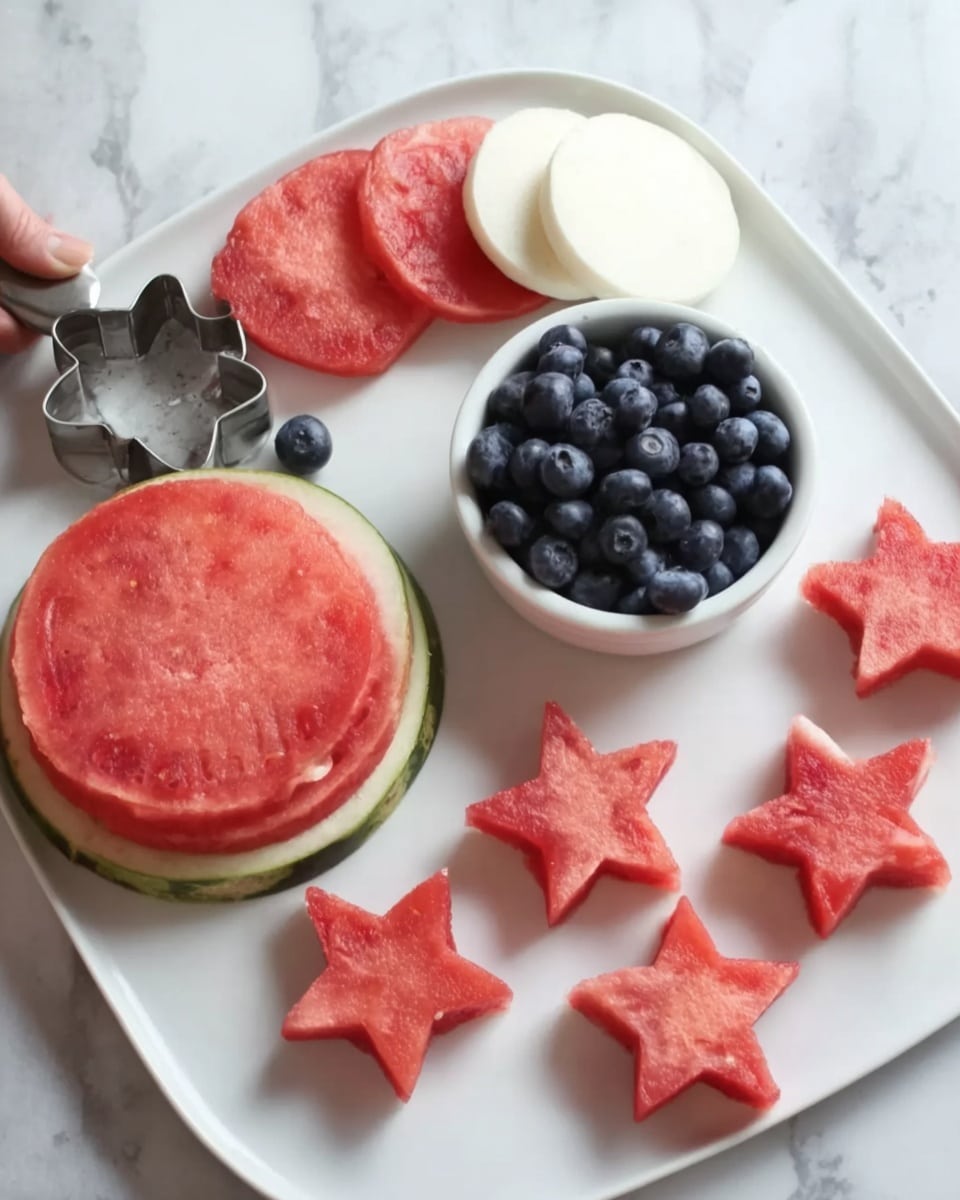 The image shows a white plate on a white marbled surface with watermelon slices cut into star shapes. A large piece of watermelon is on the left side with a metal star-shaped cutter resting on it. Next to the watermelon is a small white bowl filled with blueberries. Below the bowl, there are three round white slices stacked slightly overlapping. On the right, there are eight small star-shaped watermelon pieces placed randomly. A woman's hand is partially visible at the edge of the image. Photo taken with an iphone --ar 4:5 --v 7