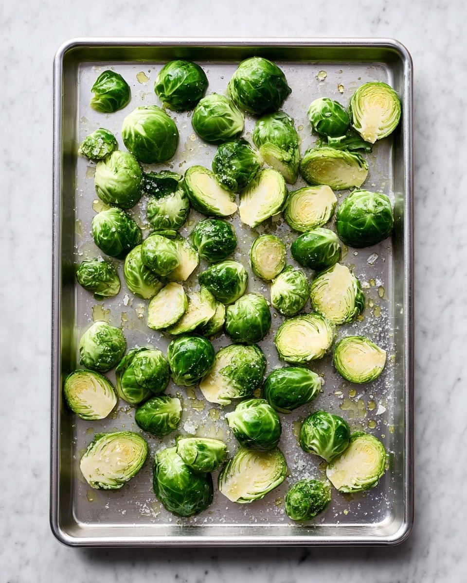 A metal baking tray is covered with green Brussels sprouts, some whole and some cut in halves, showing their light green and creamy white inner layers. The Brussels sprouts are scattered unevenly, with a drizzle of oil and sprinkles of coarse salt visible across the tray. The tray sits on a white marbled surface, creating a clean and fresh background. The lighting is bright, highlighting the fresh, smooth texture of the Brussels sprouts and the slight shine from the oil. photo taken with an iphone --ar 4:5 --v 7