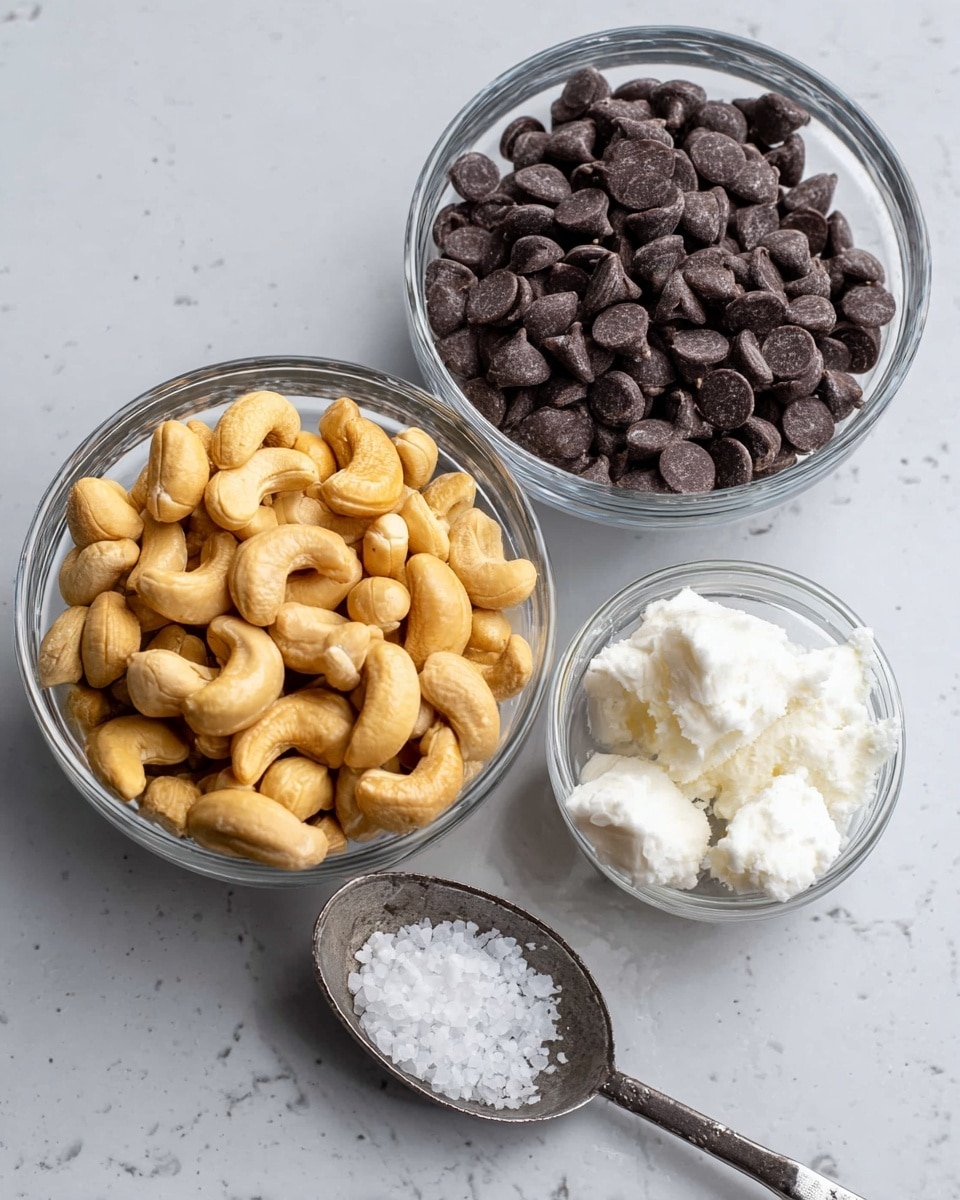 Three small clear glass bowls and a metal spoon with a scoop of white solid fat are on a white marbled surface. The largest bowl is full of light golden cashew nuts with a slightly rough texture. The second largest bowl holds many dark brown chocolate chips that are smooth and shiny. The smallest bowl contains small white coarse salt crystals. The metal spoon in the front right has a dollop of white solid fat with a soft texture. photo taken with an iphone --ar 4:5 --v 7