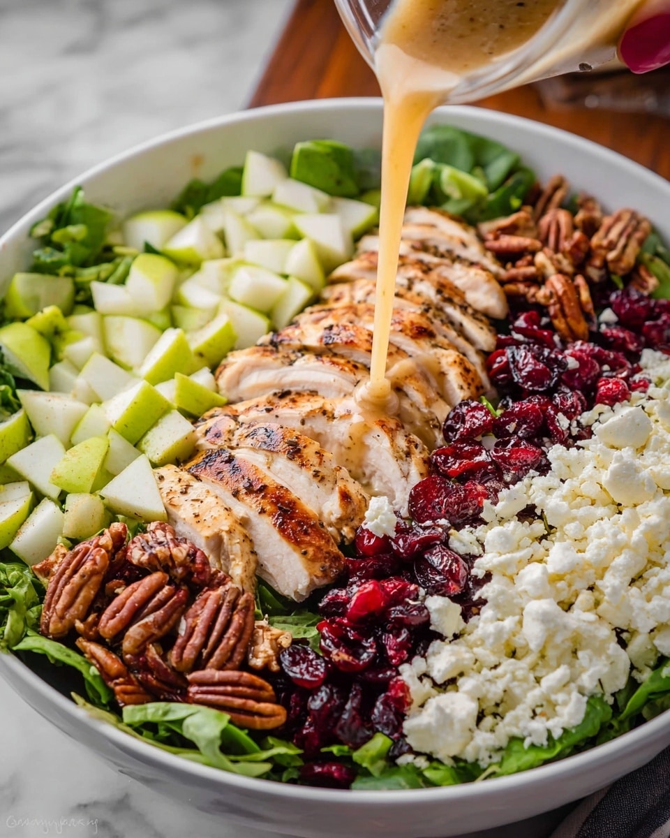 A white bowl with a salad showing five layers from left to right: diced green pear pieces, sliced golden brown grilled chicken with pepper seasoning, a layer of bright red dried cranberries, crumbled white cheese, and toasted brown pecan halves. A woman's hand is pouring a light brown dressing over the cheese and pecans. The bowl is placed on a white marbled surface photo taken with an iphone --ar 4:5 --v 7