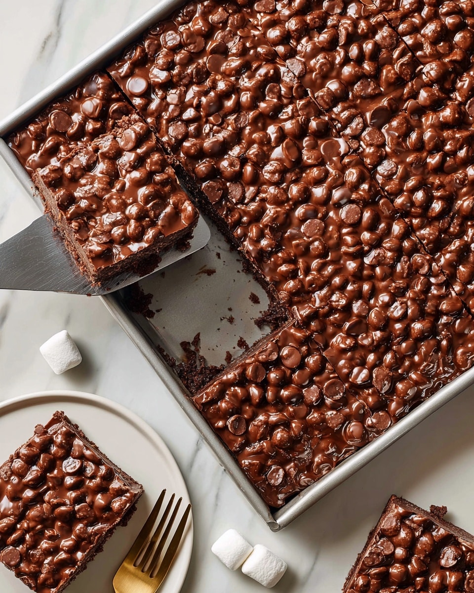A large rectangular tray holds a thick layer of chocolate dessert with a textured surface full of small, round marshmallow pieces covered in a shiny, smooth chocolate glaze. One square piece has been removed, showing a dense, dark brown inside beneath the chocolate marshmallow topping. A metal spatula lifts the cut square inside the tray. To the upper right, on a white plate, a square piece of the dessert rests next to scattered small white marshmallows. The scene is set on a white marbled surface with a white plate and gold fork partially visible in the lower left corner. Photo taken with an iphone --ar 4:5 --v 7