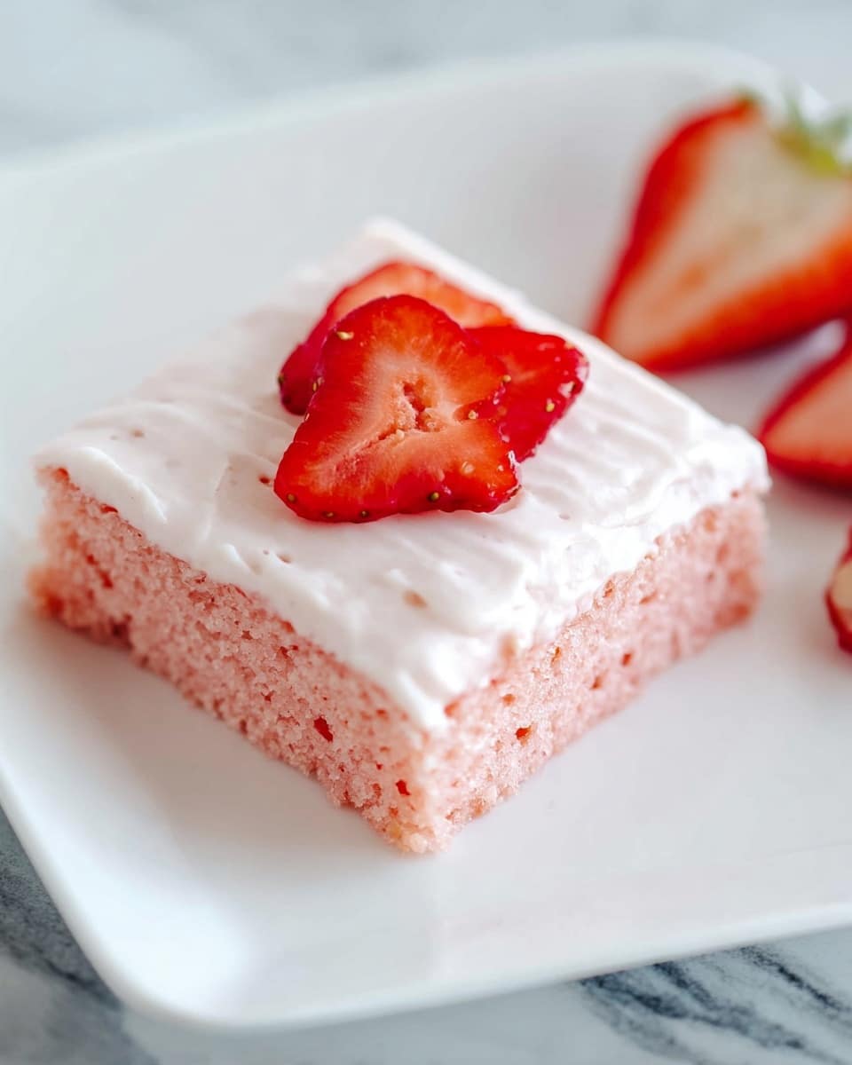 A square piece of pink cake is placed on a white plate, with two layers visible: the bottom layer is a soft, pink cake with small air bubbles, and the top layer is a light, smooth white frosting spread evenly. On top of the frosting, there are three red strawberry slices arranged in a small cluster. In the background, two strawberry halves with white inner flesh and red outer skin rest on the plate. The plate sits on a white marbled surface. photo taken with an iphone --ar 4:5 --v 7