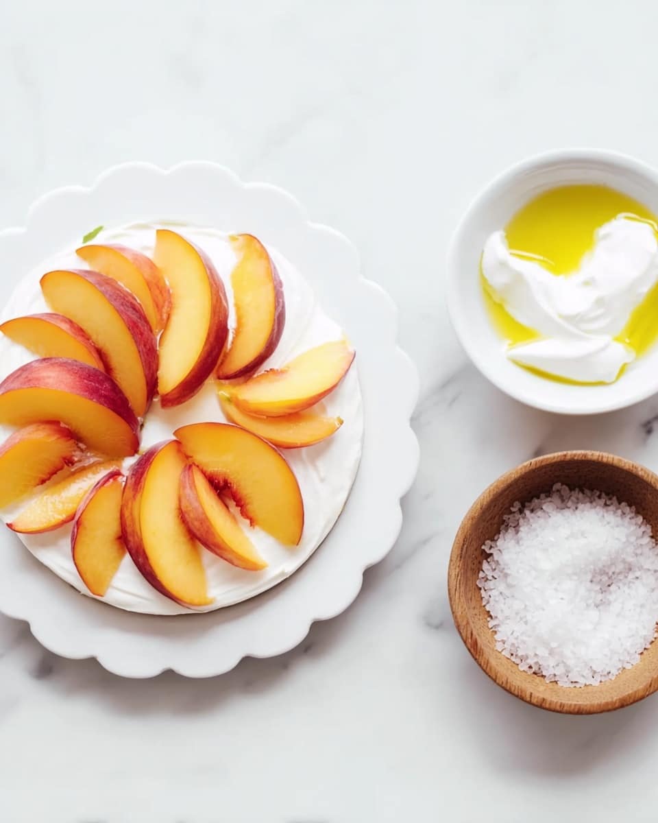 A white scalloped-edged plate holds a dessert with two main layers: the bottom layer is smooth and white, likely cream or yogurt, and the top layer is decorated with peach slices arranged in a circular pattern, showing a vibrant orange and yellow color with red edges. To the right of the plate, there is a small white bowl with dollops of white cream drizzled slightly with yellow olive oil on a white marbled surface. Below it is a small wooden bowl filled with coarse white salt. The composition is bright and clean, with a minimalist style. Photo taken with an iphone --ar 4:5 --v 7