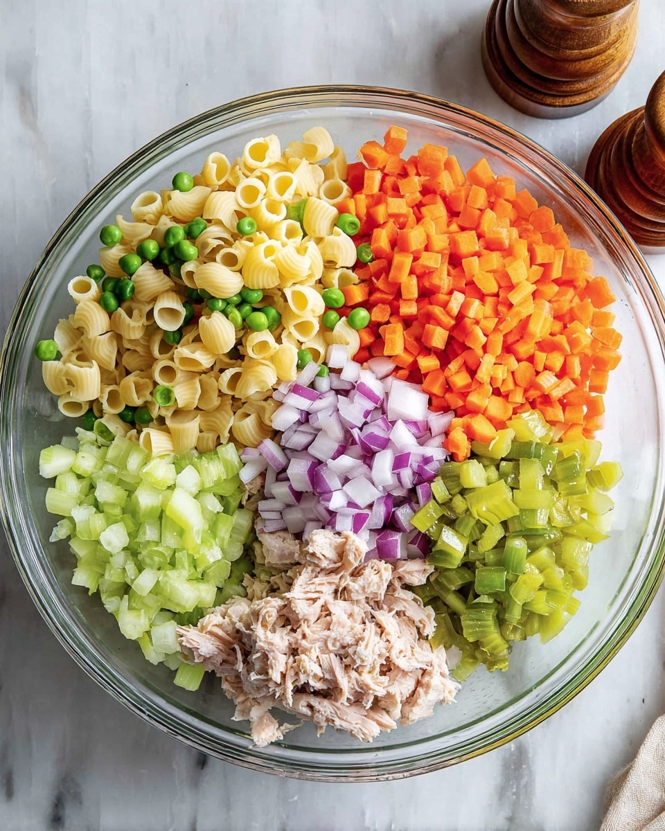 A clear glass bowl sits on a white marbled surface filled with five main ingredients arranged in separate sections. The top left section has small yellow pasta shells mixed with a few green peas. To the right, finely chopped bright orange carrots occupy a large section. Below the carrots, a smaller amount of finely chopped purple and white onions is seen. The bottom right has green diced pickles next to a small portion of light brown shredded tuna. The bottom left section is full of pale green chopped celery. Two wooden pepper mills can be seen in the top right background. photo taken with an iphone --ar 4:5 --v 7