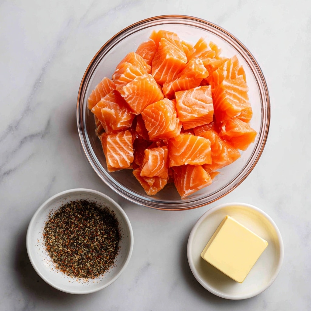 A clear glass bowl filled with bright orange salmon fillet cubes that have white marbling lines, placed on a white marbled texture surface. Below the glass bowl, a small white bowl is filled with a coarse blackened seasoning mix, which has shades of brown and red. To the right of the salmon bowl, a small white bowl holds a square piece of pale yellow butter. The background is a clean white marble with gentle gray veins. Labels in bold magenta text identify the salmon fillets, blackened seasoning, and butter on the image. photo taken with an iphone --ar 4:5 --v 7