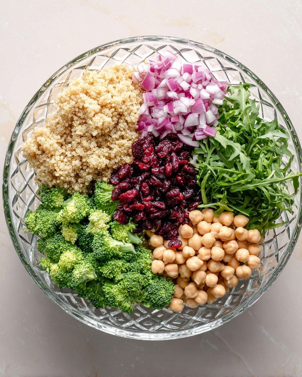 A clear glass bowl with a diamond pattern holds a salad divided into six sections: light tan quinoa in the top left, small diced red onions next to it on the top, dark green arugula occupying the top right, deep red chopped dried cranberries below the arugula, light beige round chickpeas on the bottom center, and bright green broccoli florets to the left of the chickpeas. The bowl is placed on a white marbled surface. photo taken with an iphone --ar 4:5 --v 7
