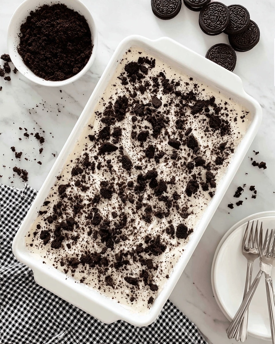 A close-up of a square chocolate layered dessert on a white plate with a white marbled surface underneath. The dessert has four clear layers: the bottom layer is a dark chocolate crumb crust with rough texture; above that is a thin creamy white layer; followed by a thick dark chocolate pudding layer with a smooth and glossy texture; the top layer is a fluffy white whipped cream sprinkled evenly with crumbled dark chocolate cookies. A woman's hand with a fork is lifting a piece from the front right side, showing the layers clearly. In the blurred background, there is a similar piece of dessert on another white plate and a white bowl filled with chocolate cookies. The photo taken with an iphone --ar 4:5 --v 7