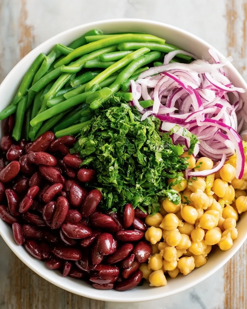 The image shows a white bowl filled with four main layers of food, each separated clearly. On the left side, there are bright green chopped green beans, positioned vertically. Next to the green beans in the center is a pile of dark green chopped herbs. Surrounding the herbs on the lower left and center are shiny red kidney beans. On the right side, there are round, yellowish chickpeas, and above those are thinly sliced purple onion strips placed loosely on top. The bowl is on a white marbled surface. Photo taken with an iphone --ar 4:5 --v 7