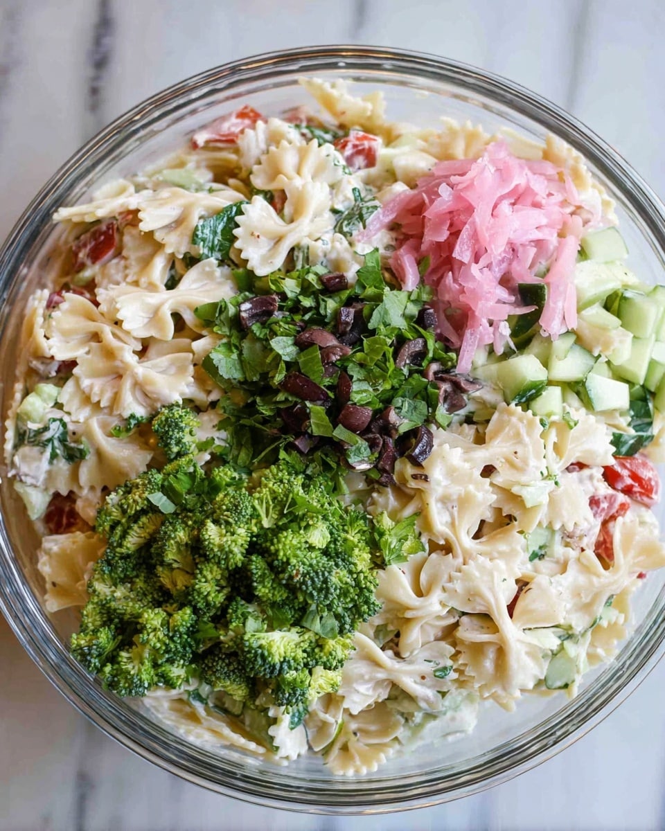 The image shows a clear glass bowl filled with a layered pasta salad. The bottom layer is made of white bowtie pasta mixed with creamy dressing, small pieces of red tomato, and green cucumber. On top of the pasta, there are bright green chopped leafy herbs, dark chopped olives, and a small pile of pink pickled onions. Around the edge of the bowl, there are fresh, bright green broccoli florets adding texture. The bowl is placed on a white marbled surface. Photo taken with an iphone --ar 4:5 --v 7