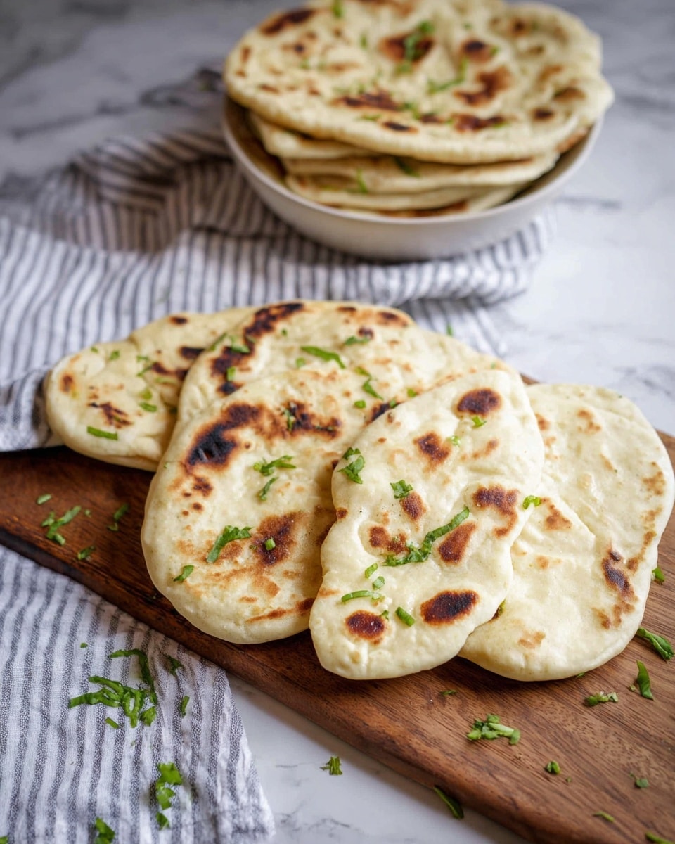 The image shows a white plate on a white marbled surface filled with several pieces of flatbread stacked in a slight messy pile. The flatbread has a light cream color with darker brown toasted spots and small green herb bits sprinkled on top, giving a fresh look. In the background, there is a blurred wooden board with more flatbread pieces and some green herbs, adding depth to the photo. The overall texture of the flatbread looks soft and slightly fluffy with playful toasting marks. Photo taken with an iphone --ar 4:5 --v 7