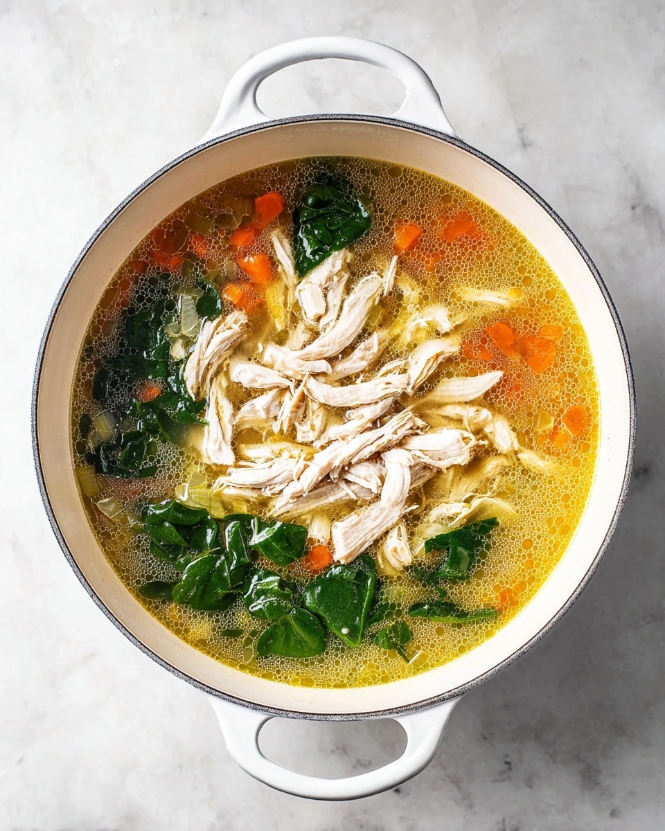 A white pot filled with a warm soup showing three main layers: the bottom layer is a golden broth with small bubbles and pieces of orange carrot and light green celery visible under the surface, the middle layer has bright green spinach leaves floating on top, and the top layer holds shredded white chicken pieces spread across the center. The pot sits on a white marbled surface, and the image is taken from above, focusing clearly on the textures and colors in the pot photo taken with an iphone --ar 4:5 --v 7