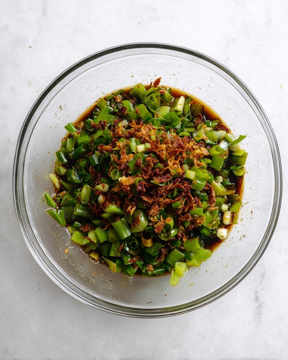 A clear glass bowl sits on a white marbled surface, filled with a mix of chopped green onions and small crispy brown fried shallots. The green onions are bright and fresh with varied sizes of short, chopped pieces, while the fried shallots add a crunchy texture and deep brown color. The ingredients are coated lightly in a dark, soy-based sauce that pools slightly at the bottom of the bowl, giving a glossy look to the mix. The bowl is viewed from above, showing the mixture evenly spread across the inside. photo taken with an iphone --ar 4:5 --v 7