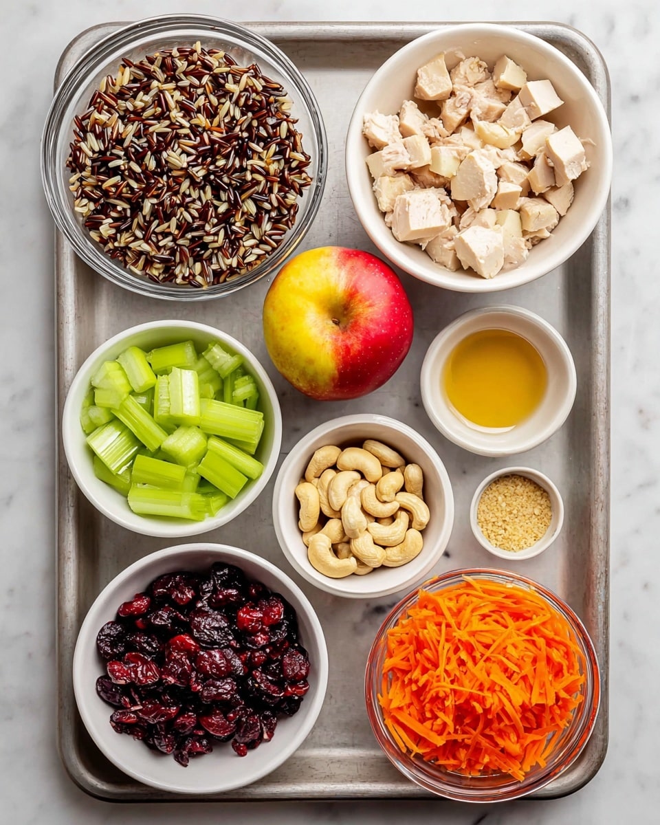 A top view of a metal tray holding small white bowls and one clear glass bowl with various ingredients, all on a white marbled surface. The clear bowl on the top left is full of cooked wild rice, a mix of dark brown and beige grains with a slightly rough texture. To the right is a white bowl filled with cubed cooked chicken, pale with some seasoning visible. Next to it is a shiny, red apple with yellow highlights. Below the apple are two small white bowls with light golden liquids. The top middle white bowl holds whole cashew nuts, creamy beige and smooth. At the bottom left is a white bowl of bright green sliced celery pieces, rough texture. Near it, another white bowl contains dark red dried cranberries, wrinkled and shiny. Below those bowls is a large white bowl with shredded bright orange carrots. The lowest small white bowl holds a small amount of coarse beige mustard. All bowls are neatly arranged on the tray. photo taken with an iphone --ar 4:5 --v 7