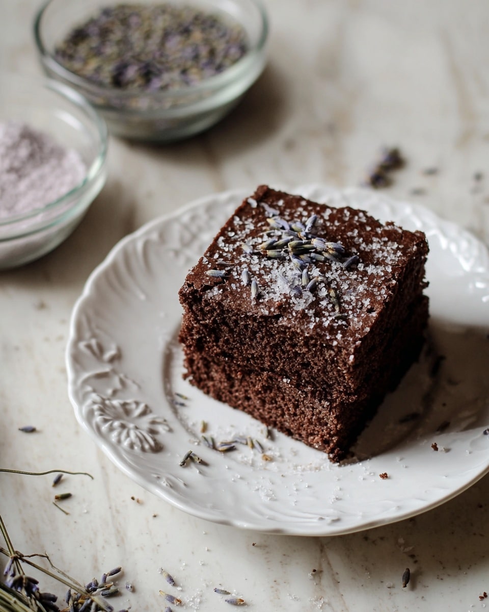 Two square layers of dark brown chocolate cake stacked on a white plate with a raised floral edge, sprinkled with coarse white sugar and small dried lavender flowers on the top layer. Around the plate, there are scattered lavender pieces and crumbs. In the background, there are two glass bowls filled with coarse ingredients, all placed on a white marbled surface. Photo taken with an iphone --ar 4:5 --v 7