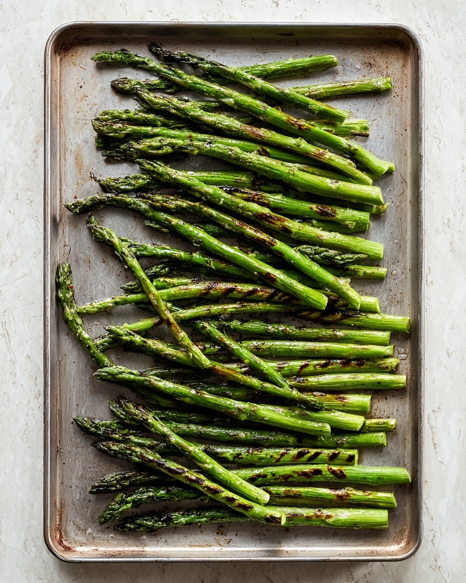 A metal tray holds about thirty grilled green asparagus stalks arranged mostly in parallel lines with some slight overlaps. The asparagus shows dark brown grill marks spaced unevenly along the bright green spears, which glisten with oil, giving the surface a shiny texture. The tray has a slightly worn look and is placed on a white marbled textured surface. photo taken with an iphone --ar 4:5 --v 7