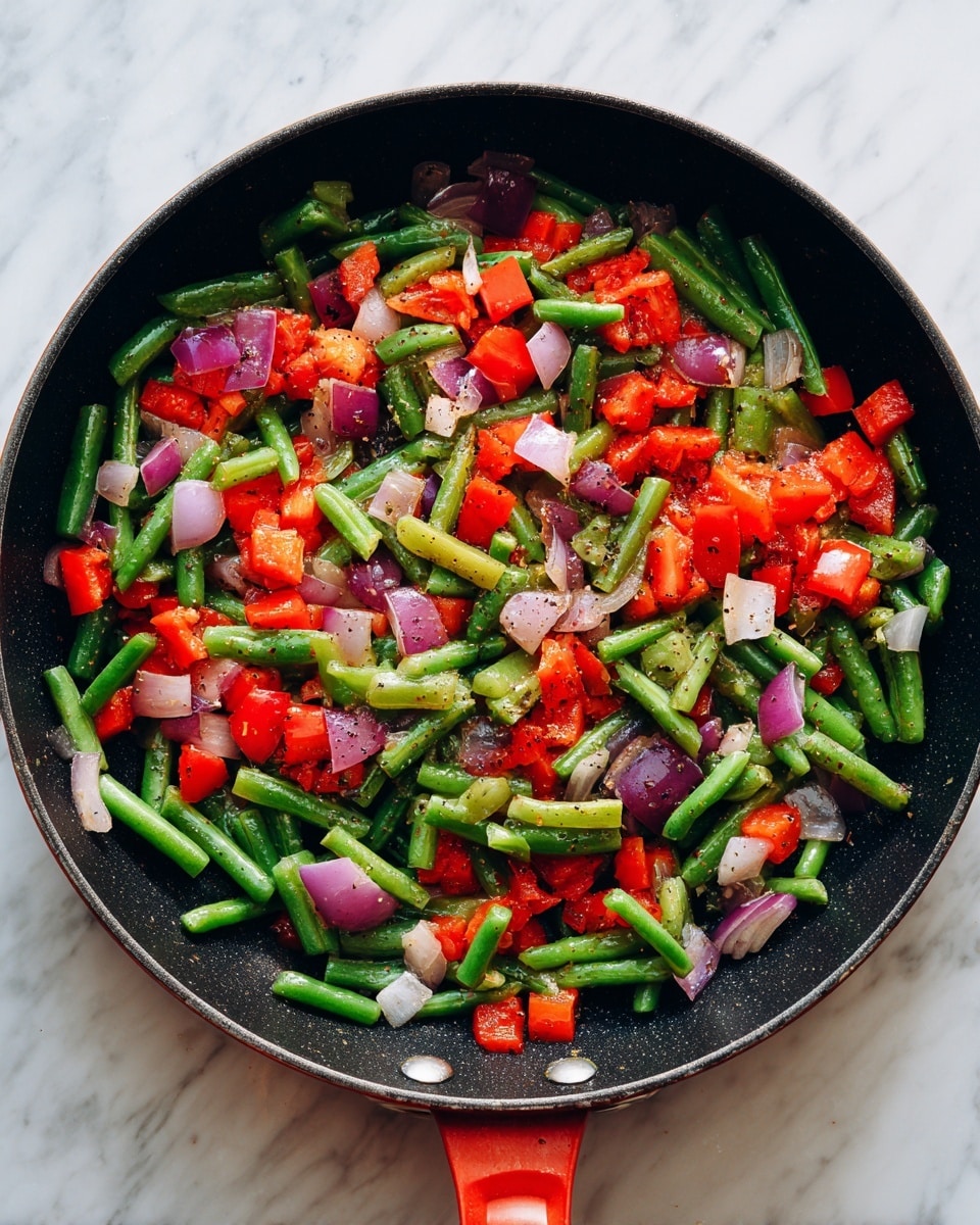 A black pan with a red handle sits on a white marbled surface, filled with a colorful mix of cooked vegetables. The dish has three main layers: a scattered layer of green beans cut into small pieces, bright red bell pepper cubes, and diced onion pieces showing light purple and white tones. The vegetables are slightly shiny, indicating they have been cooked and seasoned with visible black pepper specks. The pan is wide and round with the mix evenly spread across the surface. photo taken with an iphone --ar 4:5 --v 7