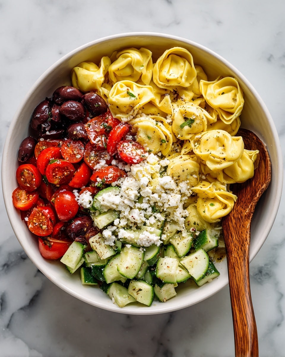 A white bowl filled with multiple layers of food, starting with a mix of small green cucumber pieces and red cherry tomato halves at the bottom, followed by a layer of black olives scattered throughout. On top of this is a layer of yellow tortellini pasta spread evenly, with some pieces overlapping the edges of the bowl. The whole dish is sprinkled with white crumbly cheese, mainly in the center. There is a wooden spoon resting on the right side inside the bowl. The bowl sits on a white marbled surface. Photo taken with an iphone --ar 4:5 --v 7
