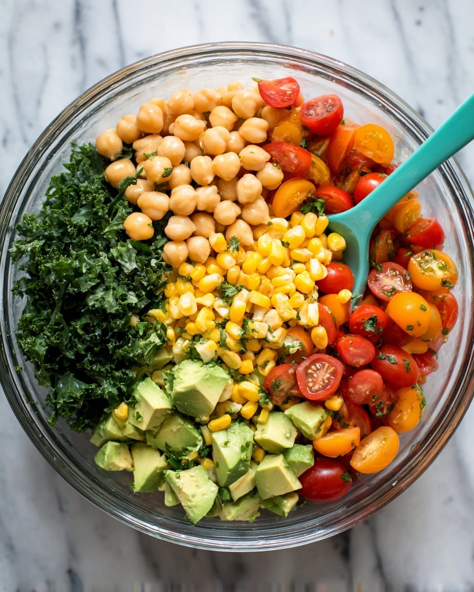 A clear glass bowl holds a colorful salad with visible layers and textures. The base layer consists of light beige chickpeas mixed with bright yellow corn kernels. On top of this, there are chopped chunks of green avocado scattered evenly across the surface. Among the avocado pieces are small, round cherry tomatoes, both red and orange, some whole and some cut in half showing their juicy inside. Dark green chopped herbs or kale form a cluster on one side of the bowl, adding more color contrast. A turquoise serving spoon rests inside the bowl, partially buried in the mix. The bowl sits on a white marbled surface. photo taken with an iphone --ar 4:5 --v 7
